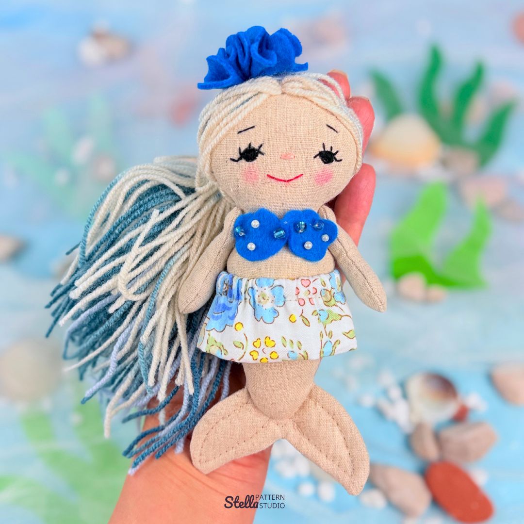 Mermaid doll with blue hair and floral outfit against a blurred underwater background