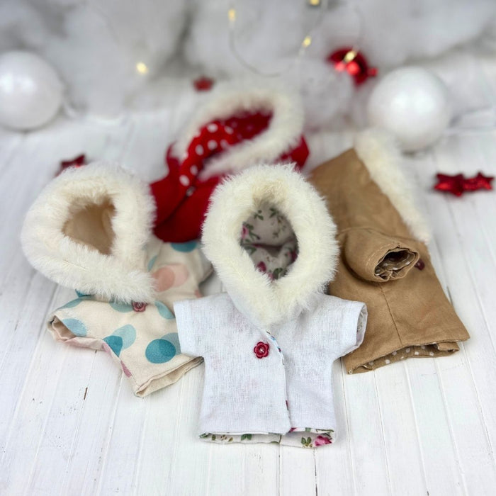 Set of baby shoes, coat, and accessories on a white surface with Christmas decorations.